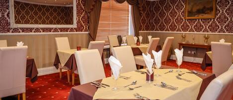 A dining area with tables set for four, chairs, and a large mirror on the wall.