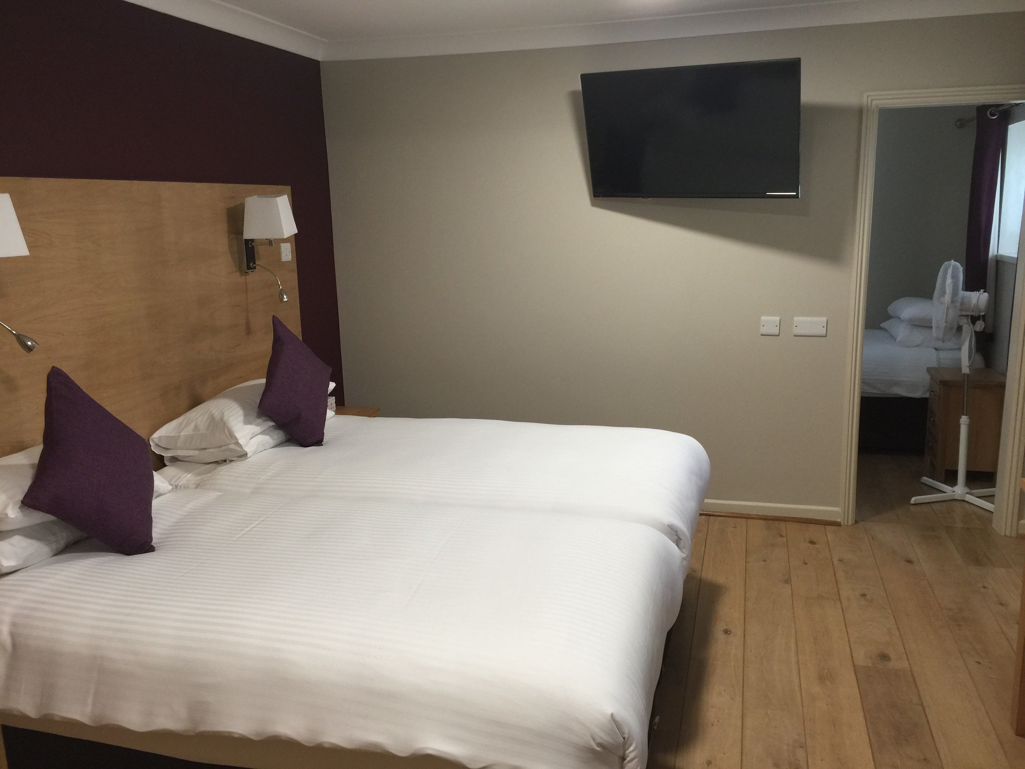 Ein Hotelzimmer mit einem großen Bett, zwei Nachttischlampen, einem an der Wand befestigten Flachbildfernseher und einem Holzboden.