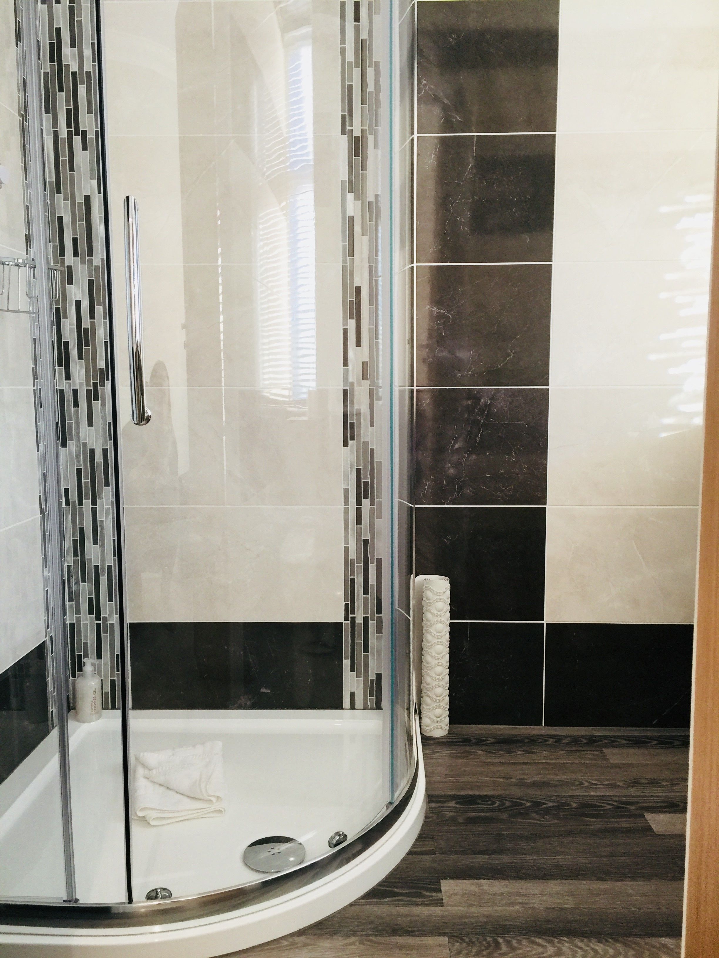 Un baño moderno con ducha de vidrio, una bañera blanca y una combinación de baldosas blancas y negras en las paredes.