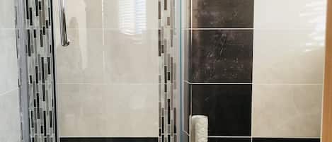 Un bagno moderno con doccia vetrata, una vasca da bagno bianca e un rivestimento a parete con piastrelle bianche e nere.
