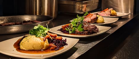 Una cocina con electrodomésticos de acero inoxidable y una variedad de platos con carnes asadas y verduras.