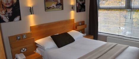 A neatly made bed with a wooden headboard, a bedside table with a phone, and wall-mounted lamps.
