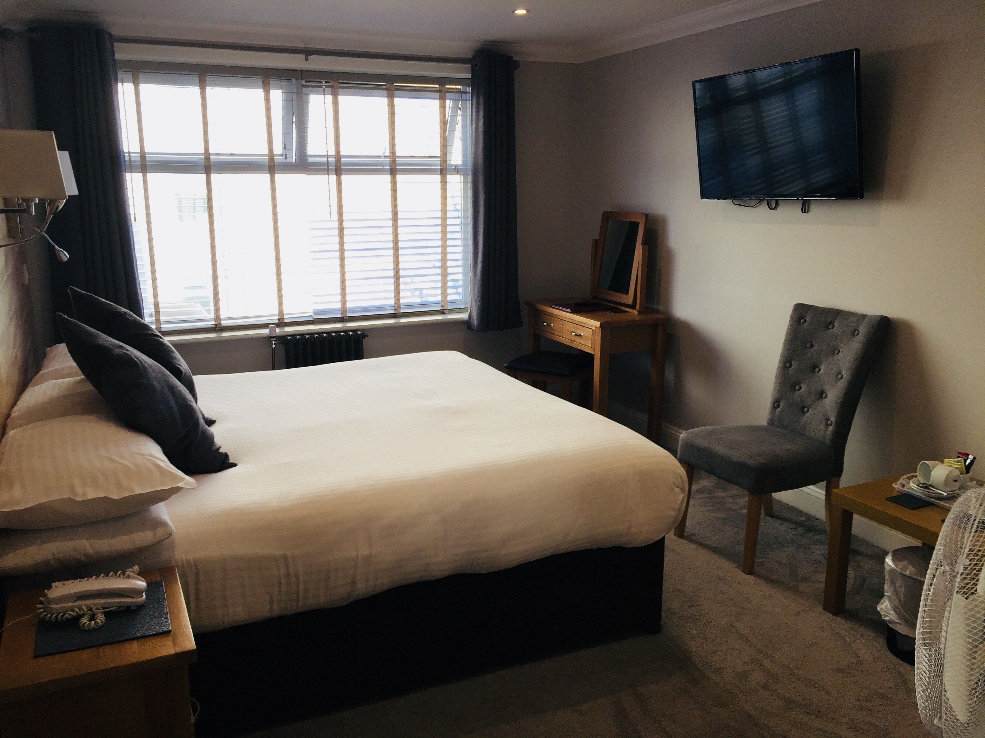 Habitación de hotel con una cama grande, un escritorio con silla, televisión montada en la pared y una ventana con persianas.