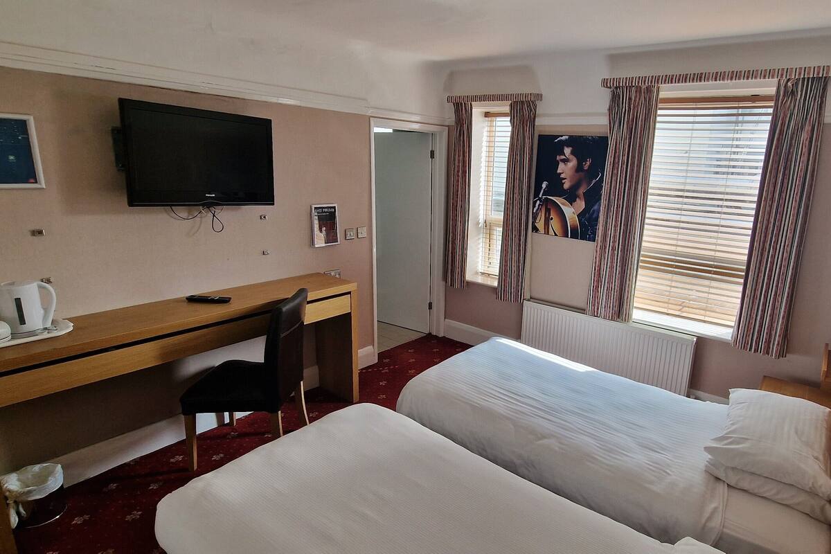 Hotellihuone, jossa on sänky, työpöytä, tuoli, televisio ja ikkuna, jossa on verhot.