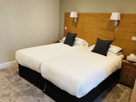 Cama doble con sábanas blancas, dos lámparas de noche, un cabecero de madera, mesita de noche con caja de pañuelos y suelo alfombrado.