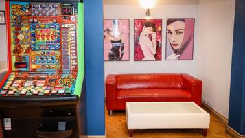 A room with a red leather sofa, a white ottoman, and a slot machine. There are three framed pictures on the wall.