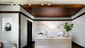 A reception area with a marble wall, a desk with a computer, a plant, and a bench. - The Ambrose (Santa Monica)