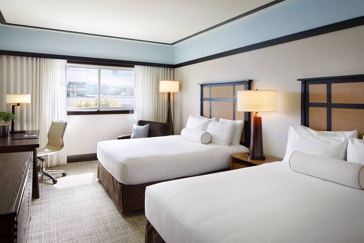A hotel room with two beds, a desk, and a chair.