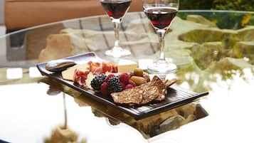 A glass table with a charcuterie board, two glasses of red wine, and a sofa with a plaid pillow in the background.