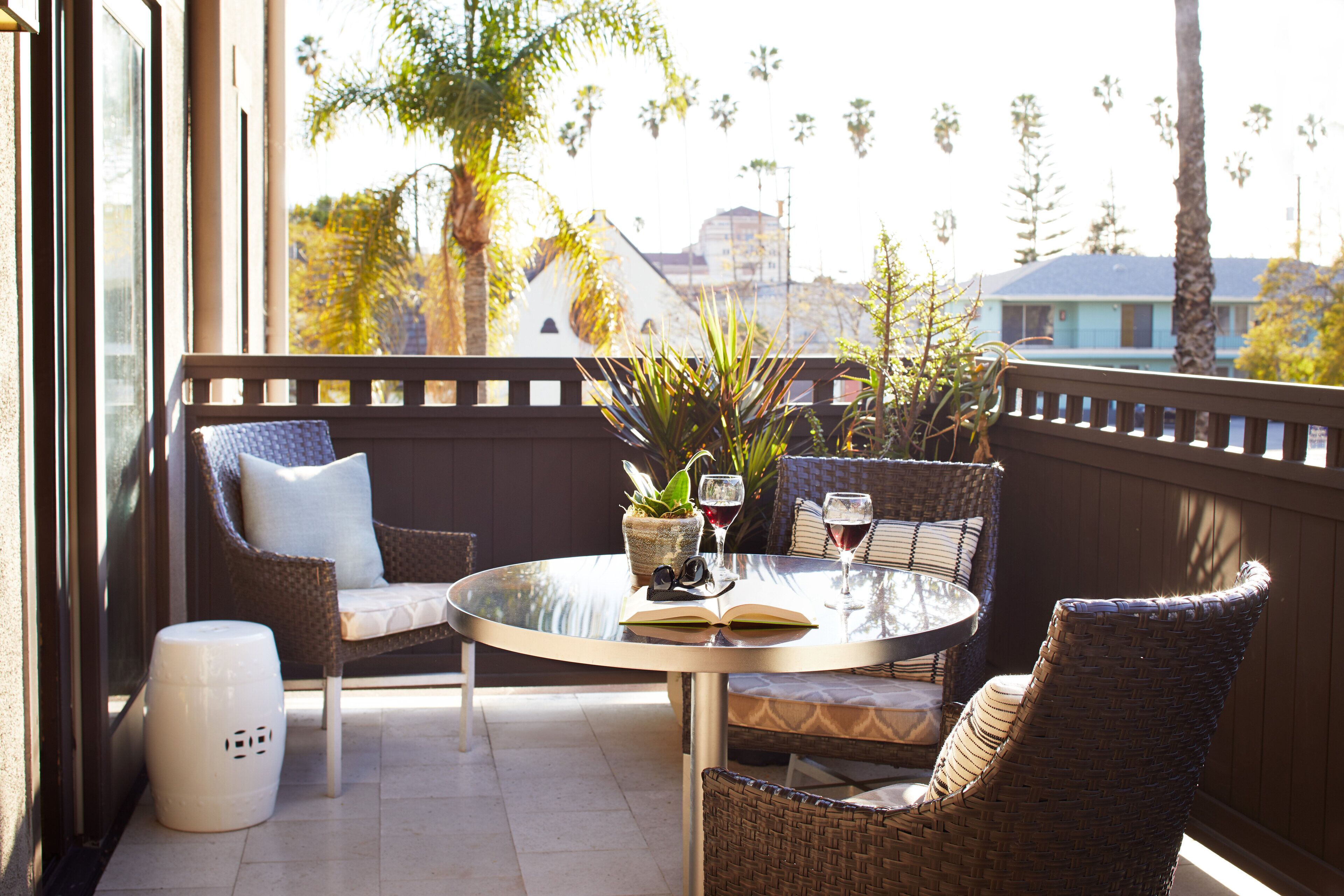Ein Balkon mit Korbmöbeln, einem Glastisch und einem Blumentopf.