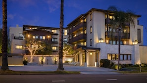 A multi-story hotel with a modern design, featuring balconies, a well-lit entrance, and a landscaped driveway. - The Ambrose (Santa Monica)