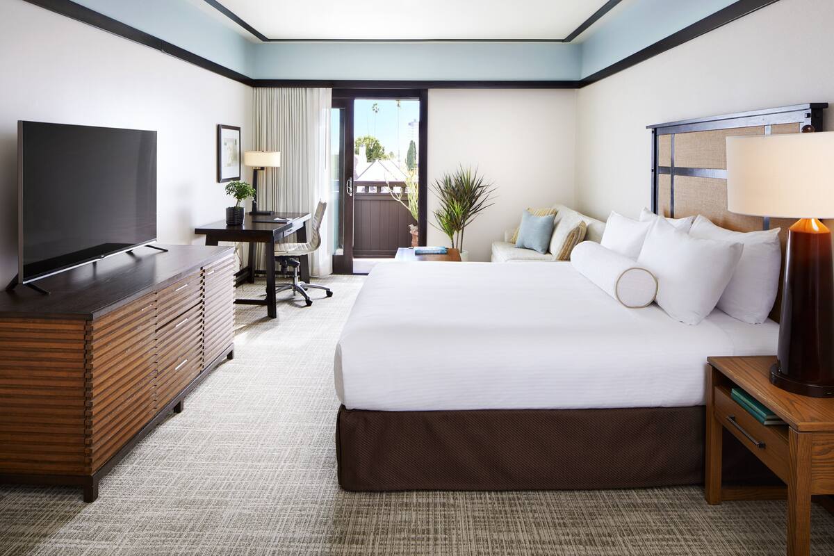 A hotel room with a large bed, a desk with a chair, a TV, and a lamp.