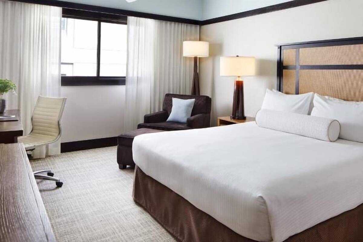 A hotel room with a large bed, two bedside lamps, a chair, a desk, and a window with curtains.