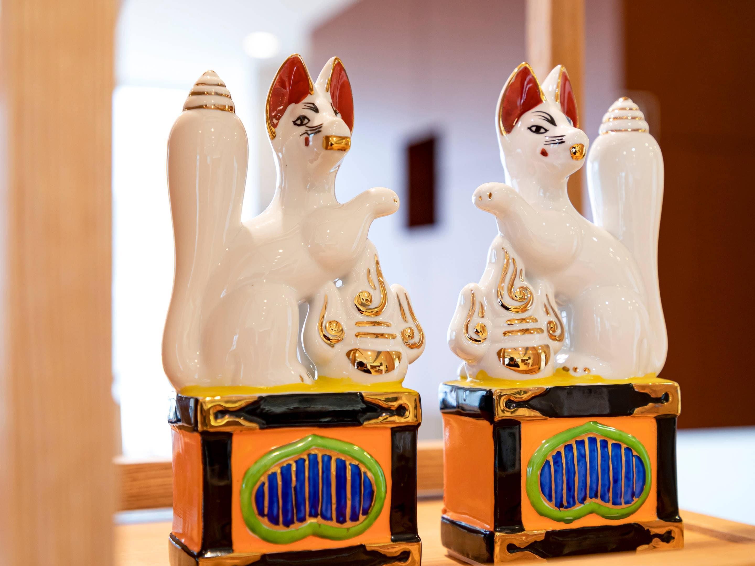 Two white ceramic cat figurines with gold accents on a colorful base.
