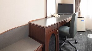 Habitación de hotel con escritorio de madera, una silla, televisor, teléfono y cubo de basura.