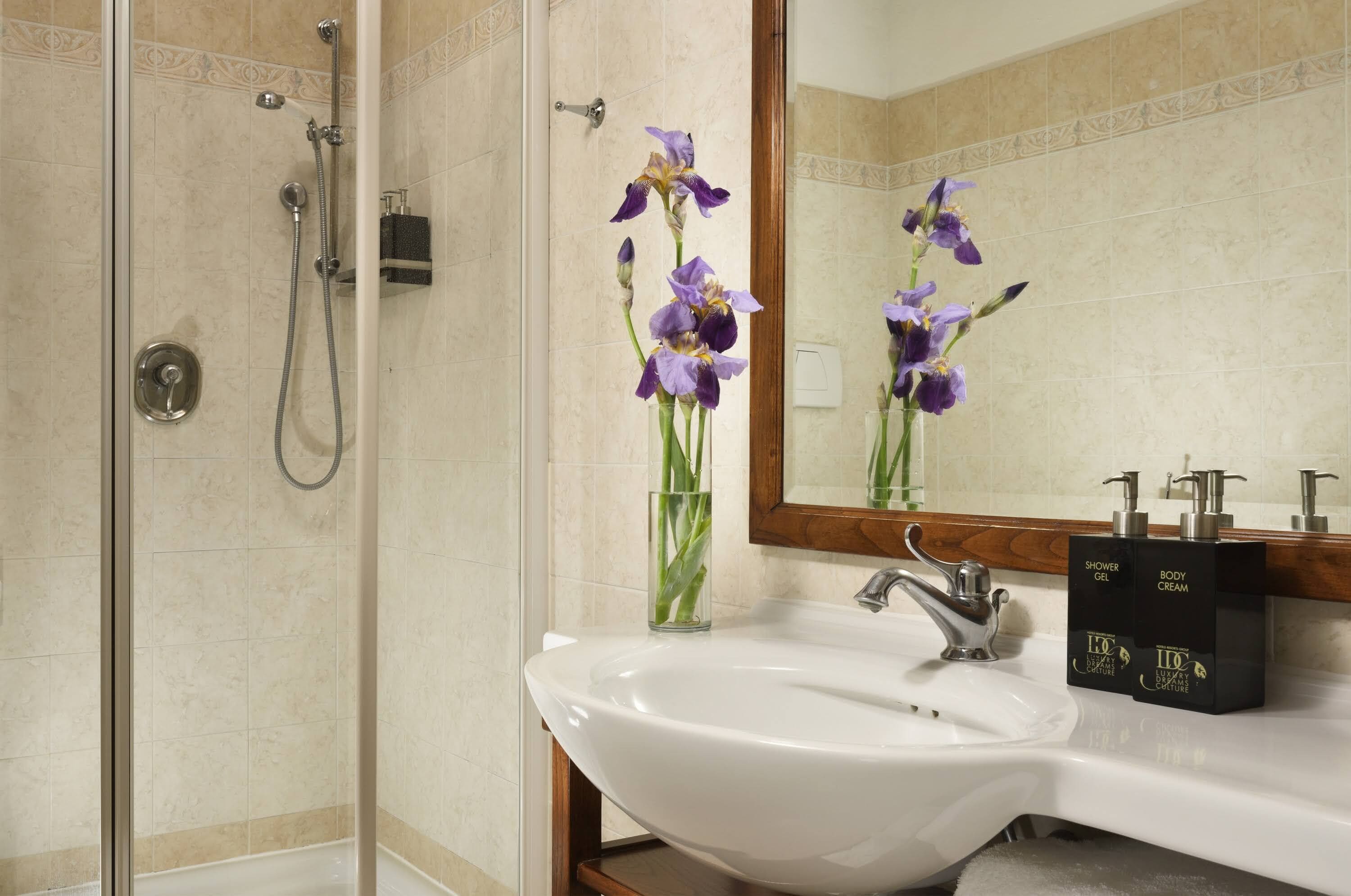A bathroom with a glass shower enclosure, a white sink, and a mirror reflecting purple flowers.