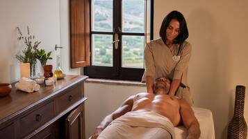 A massage therapy session in a room with a wooden cabinet, a window with a view of greenery, and a decorative vase.