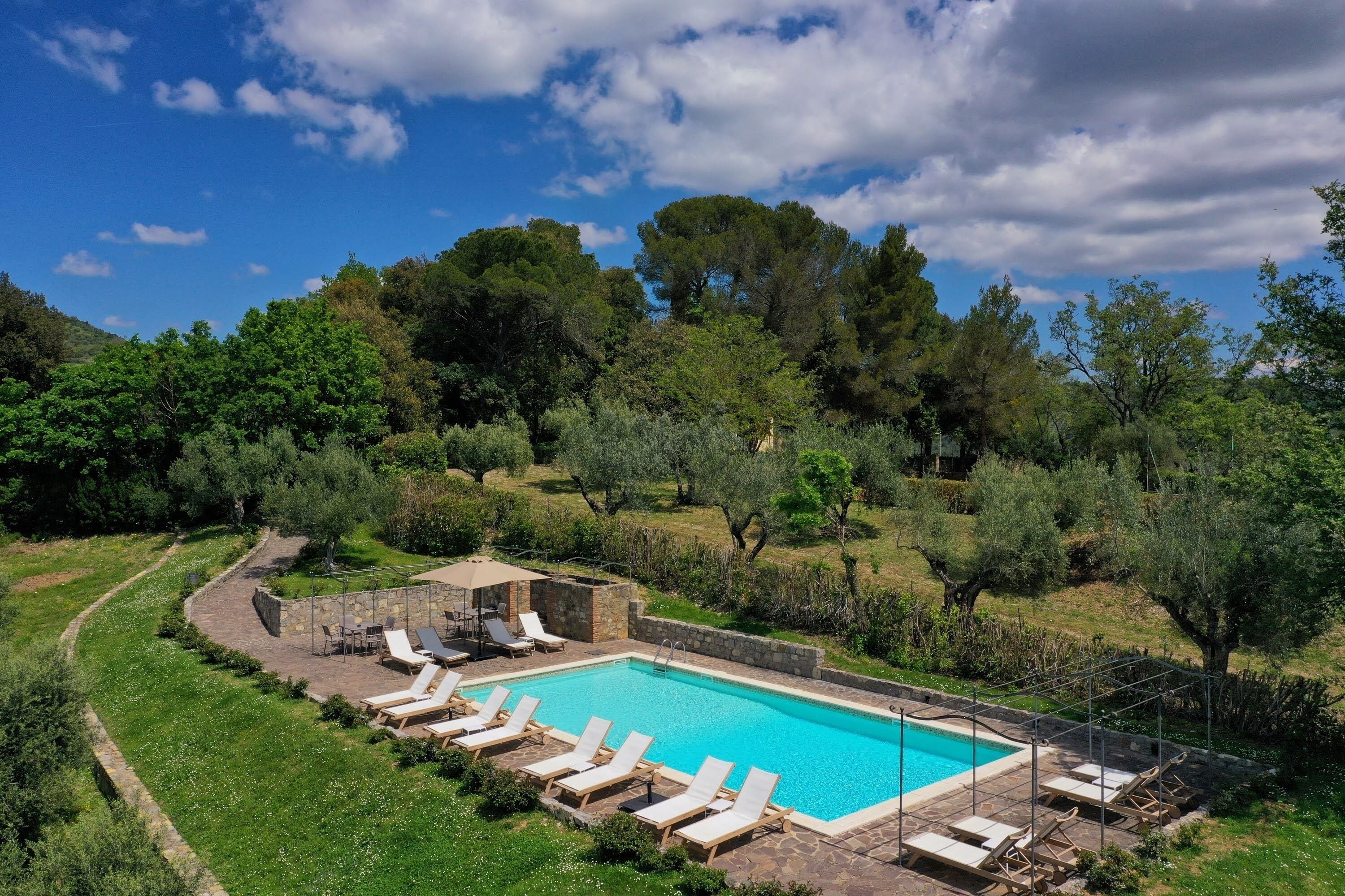 A rectangular pool with lounge chairs and a stone structure, surrounded by lush greenery and trees.