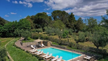 A rectangular pool with lounge chairs and a stone structure, surrounded by lush greenery and trees.