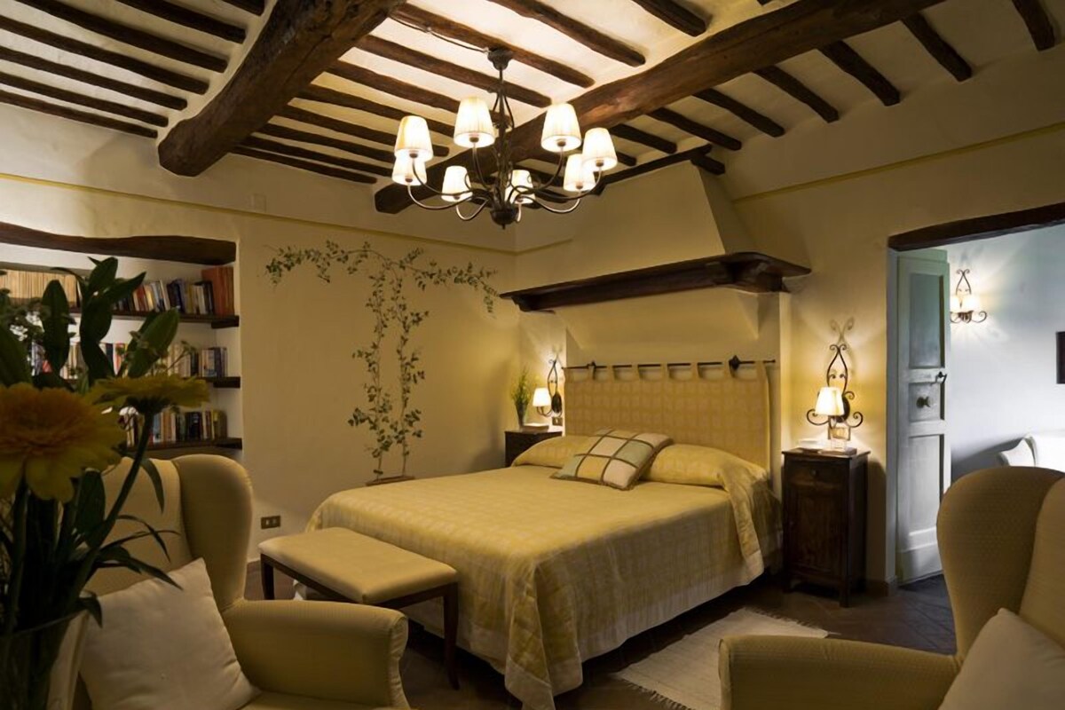 Un dormitorio acogedor con una cama grande, dos mesitas de noche, una araña y una estantería.