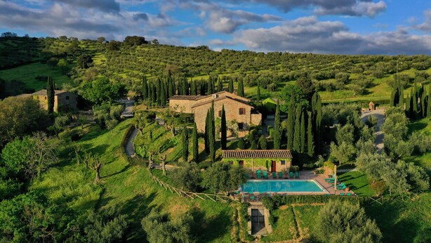 Una villa con piscina rodeada de vegetación exuberante y altos cipreses.