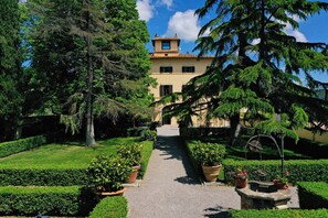 A pathway leading to a building with a tower, surrounded by well-maintained gardens and trees. - Relais Villa Monte Solare Wellness & SPA (Panicale)