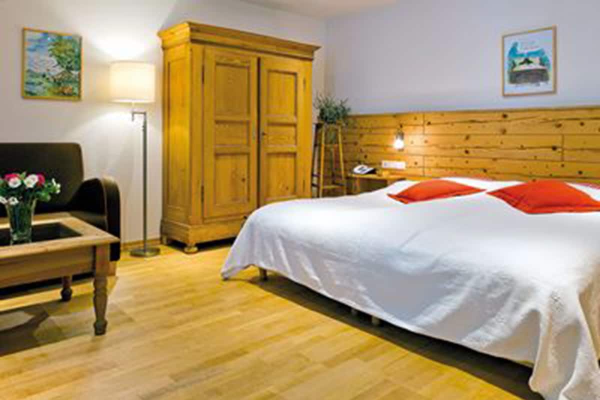 Een kamer met een bed, een houten garderobe, een bureau met een bloemenvaas en een lamp.