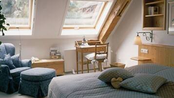 Une pièce chaleureuse avec un plafond en pente, un lit recouvert d’une couette à motifs, une chaise, une petite table et une étagère remplie de livres.