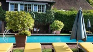 A swimming pool with lounge chairs and an umbrella, surrounded by greenery and a house in the background. - Romantik Hotel Spielweg (Münstertal)
