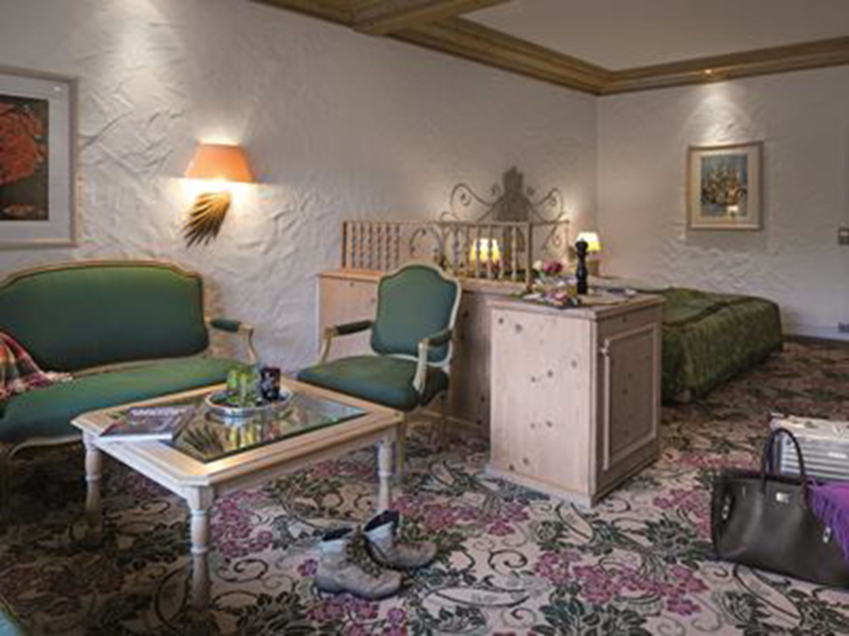 A room with a green sofa, a small table with a lamp, a cabinet, and a bed with a green cover.