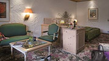 A room with a green sofa, a small table with a lamp, a cabinet, and a bed with a green cover.