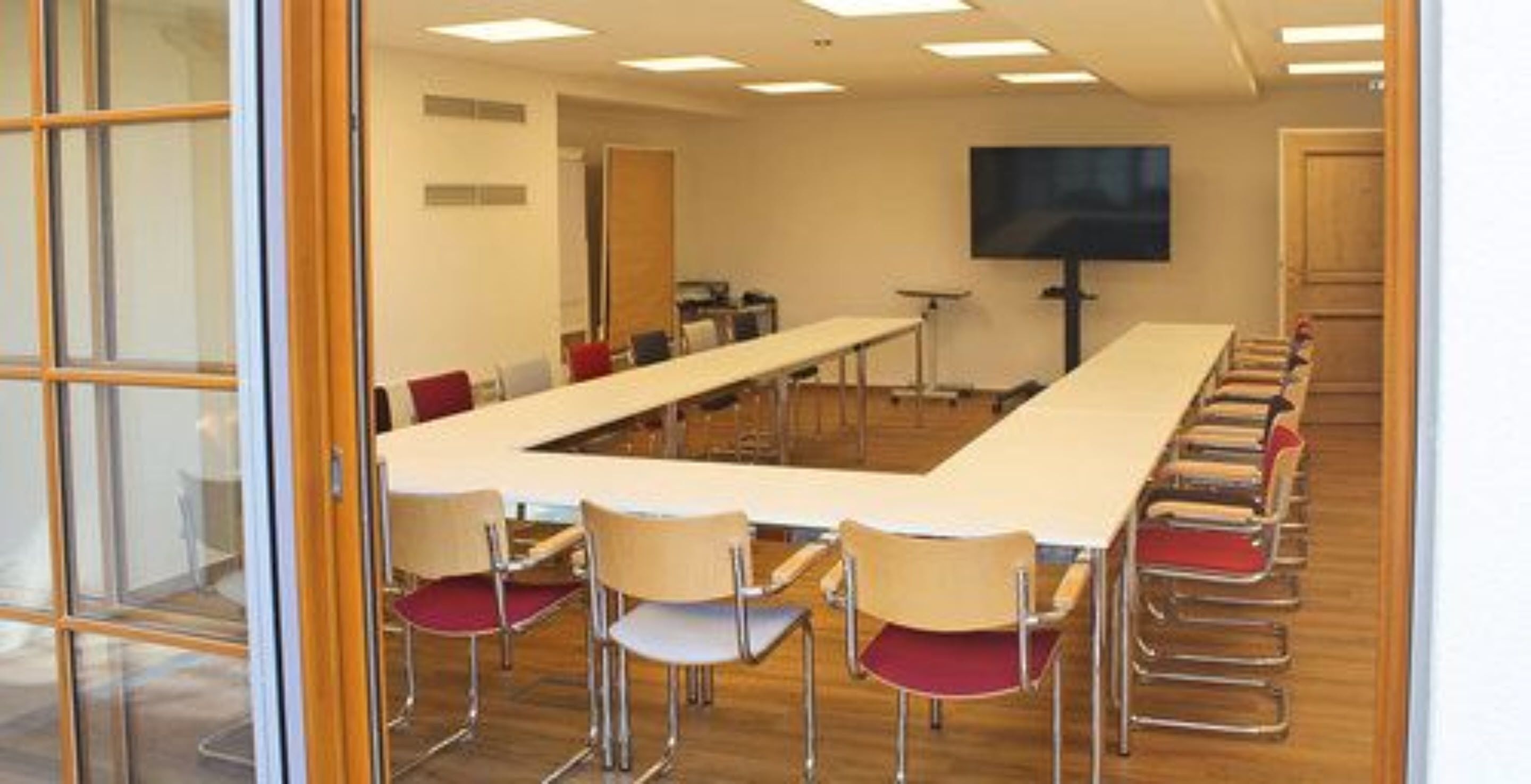 Un salón de conferencias con una larga mesa, sillas, un televisor y una puerta de madera.