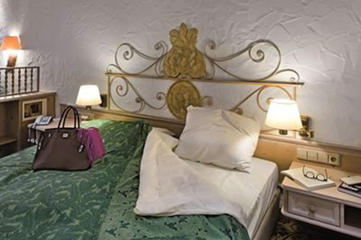 Een hotelkamer met een bed, nachtkastje, lamp, handtas en decoratief hoofdeinde.