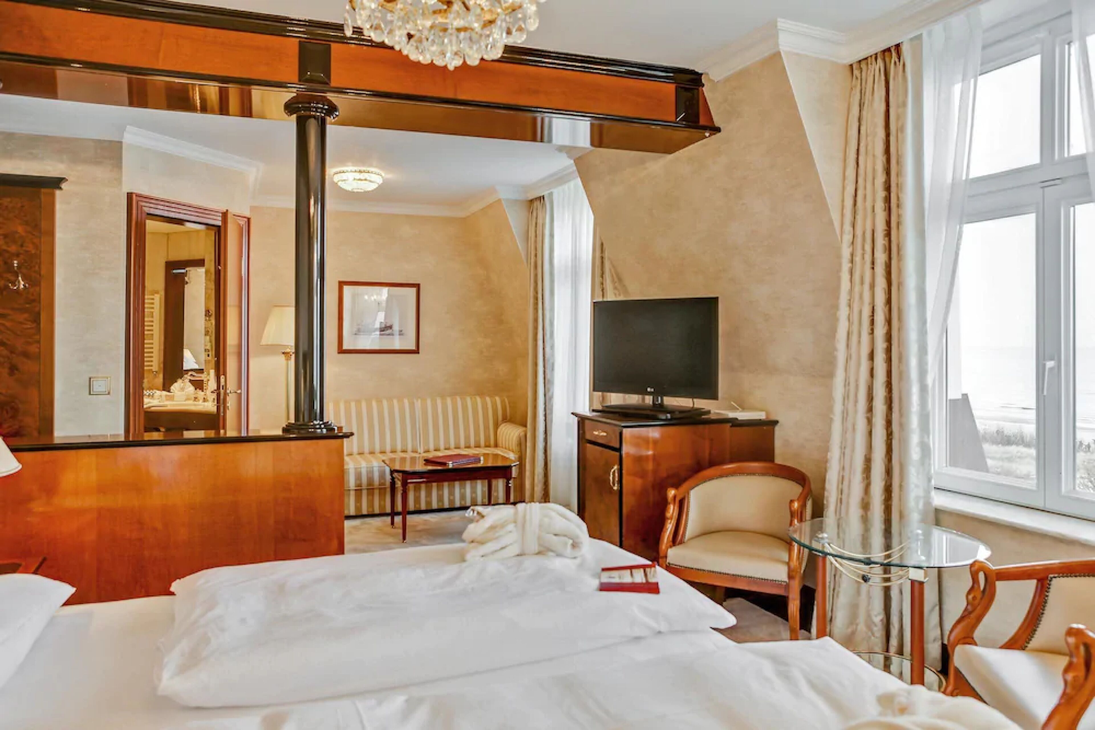 Ein Hotelzimmer mit einem großen Bett, einer Sitzecke mit Sofa und Sesseln, einem Fernseher und Blick ins Freie.