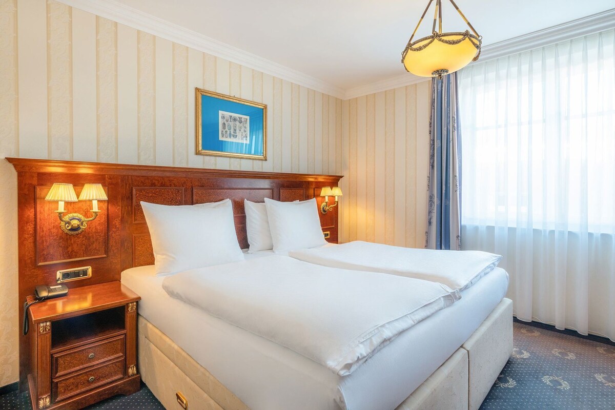 Un lit double avec une tête de lit en bois, des lampes de chevet, une table de chevet avec un téléphone et un tableau encadré au-dessus du lit.