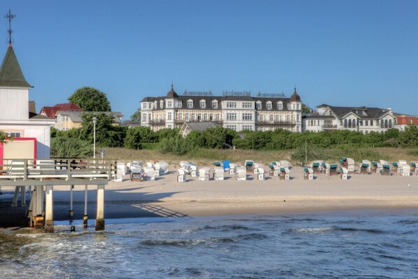 A beachfront hotel with a large building, a pier, and beach chairs.