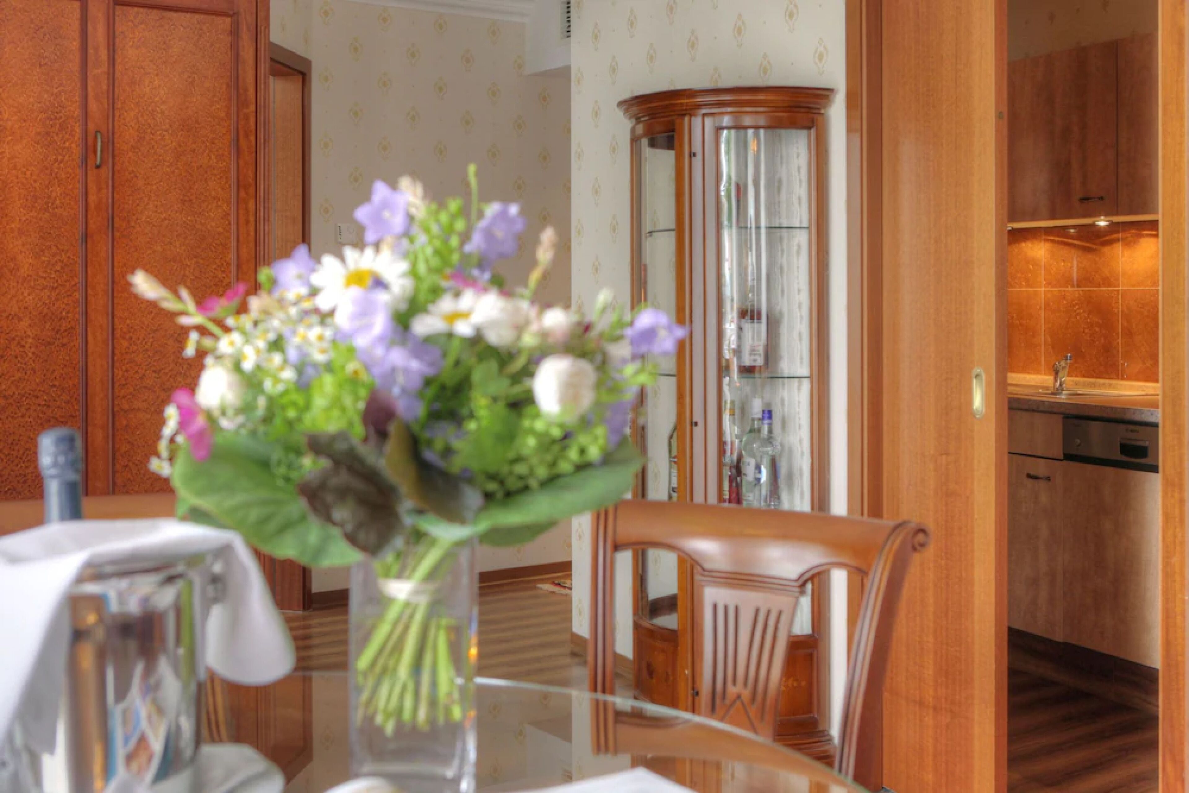 A dining area with a glass table, wooden chairs, and a vase of flowers.