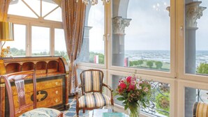 A room with a large window overlooking a body of water, a wooden chest of drawers, a striped armchair, and a glass table with a vase of flowers. - SEETELHOTEL Ahlbecker Hof (Heringsdorf)