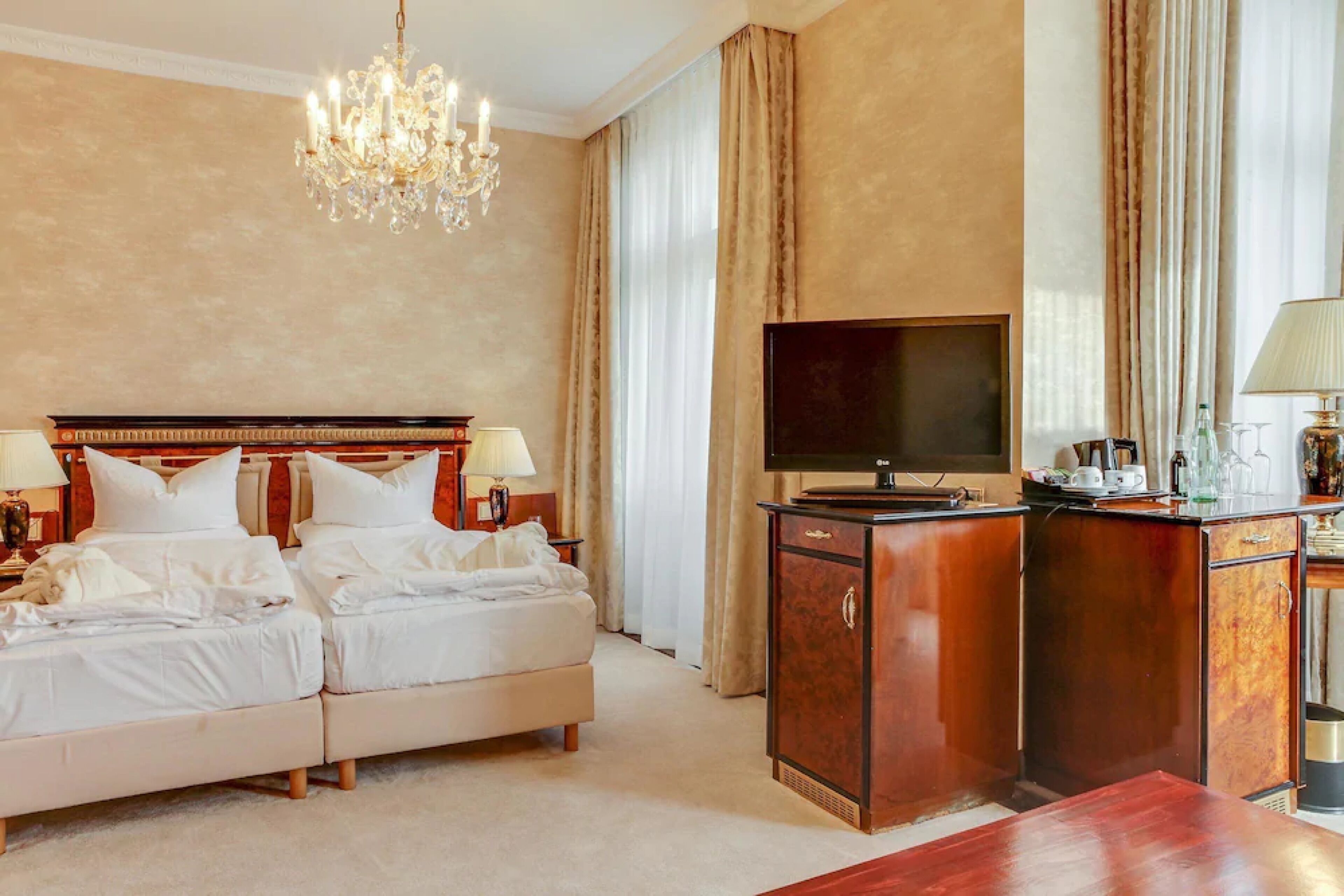 A hotel room with a double bed, a TV, a wooden cabinet, and a chandelier.