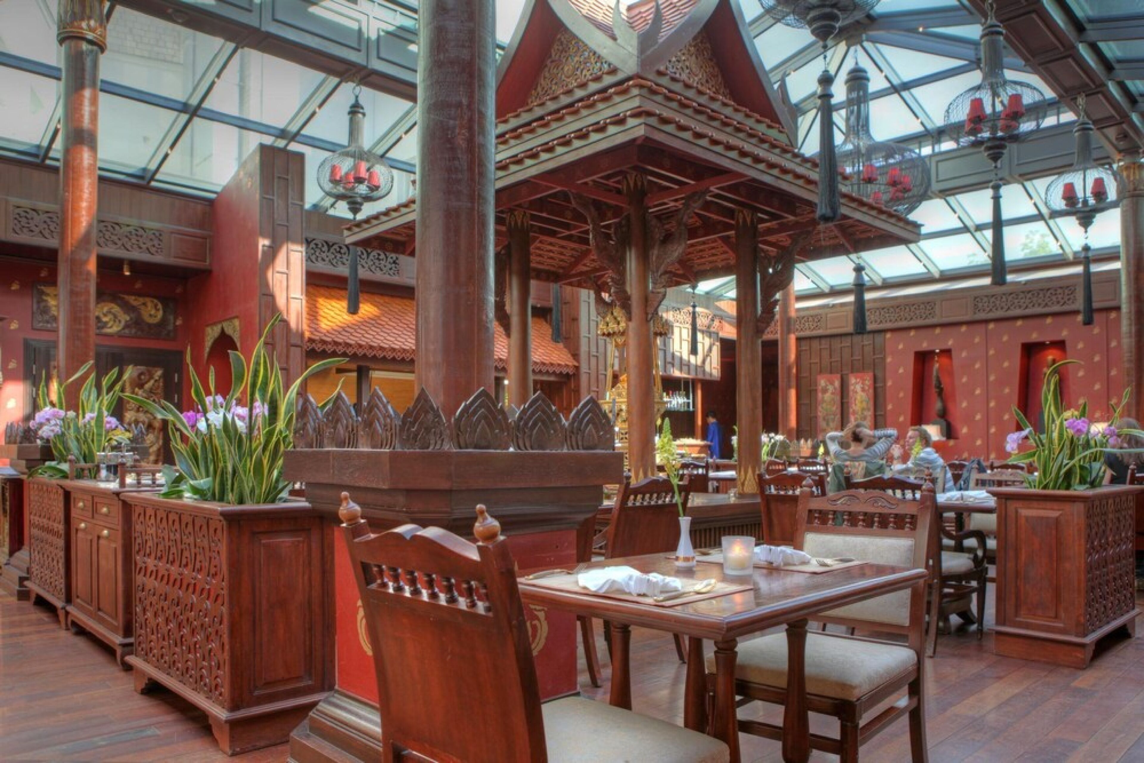 An indoor dining area with wooden furniture, a glass ceiling, and decorative plants.