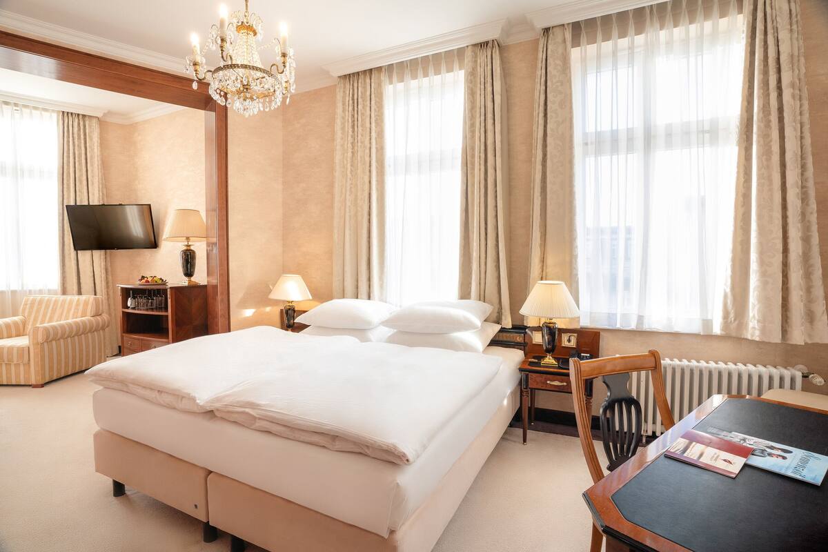 Une chambre d’hôtel avec un grand lit, une télévision, un bureau avec une chaise et un lustre.