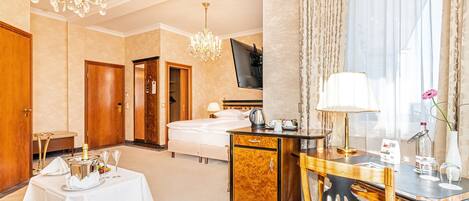 Habitación de hotel con cama, escritorio, silla, mesa con una botella y vasos, televisor y candelabro.