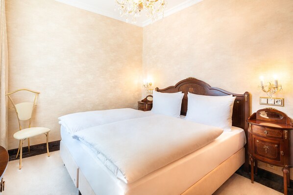 Una cama grande con sábanas blancas, una mesita de noche de madera con un teléfono y una lámpara fijada a la pared.