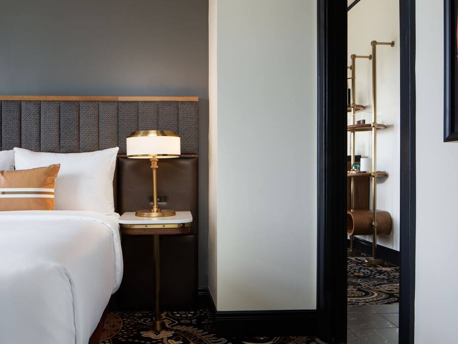 Una habitación de hotel con cama, lámpara de noche, mesita de noche y estante en la pared.