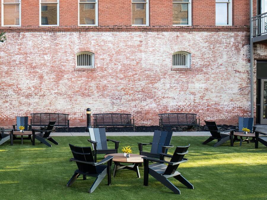 Un espacio al aire libre con sillas y mesas, un muro de ladrillo y un edificio al fondo.
