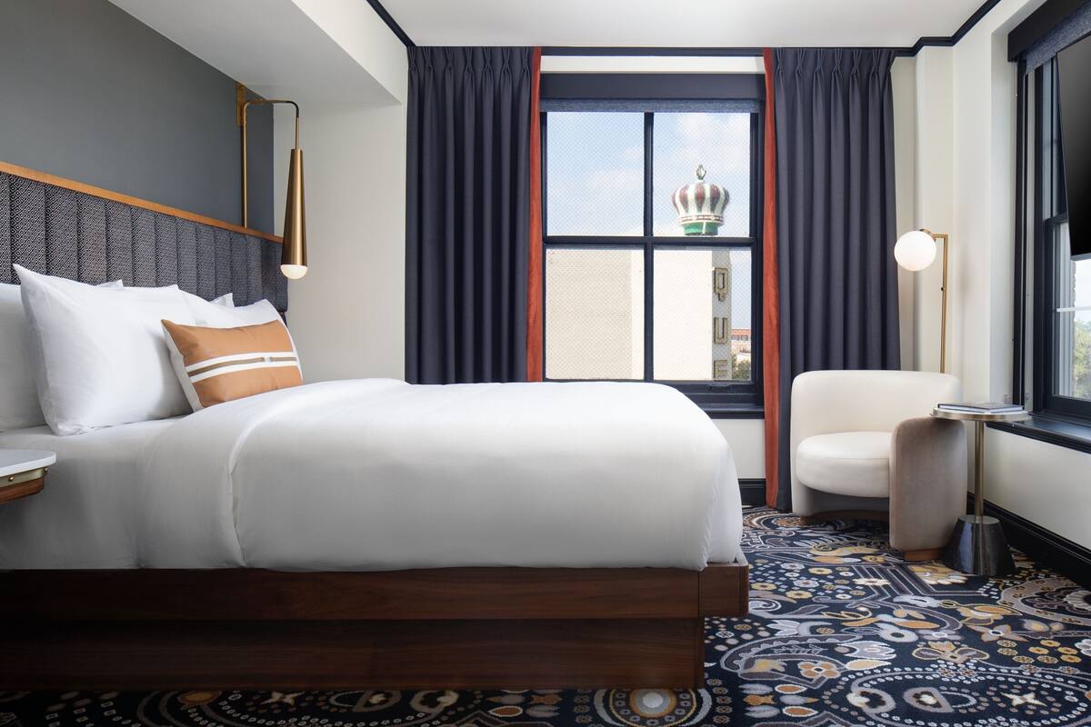 A hotel room with a large bed, a chair, a desk, and a window with curtains.