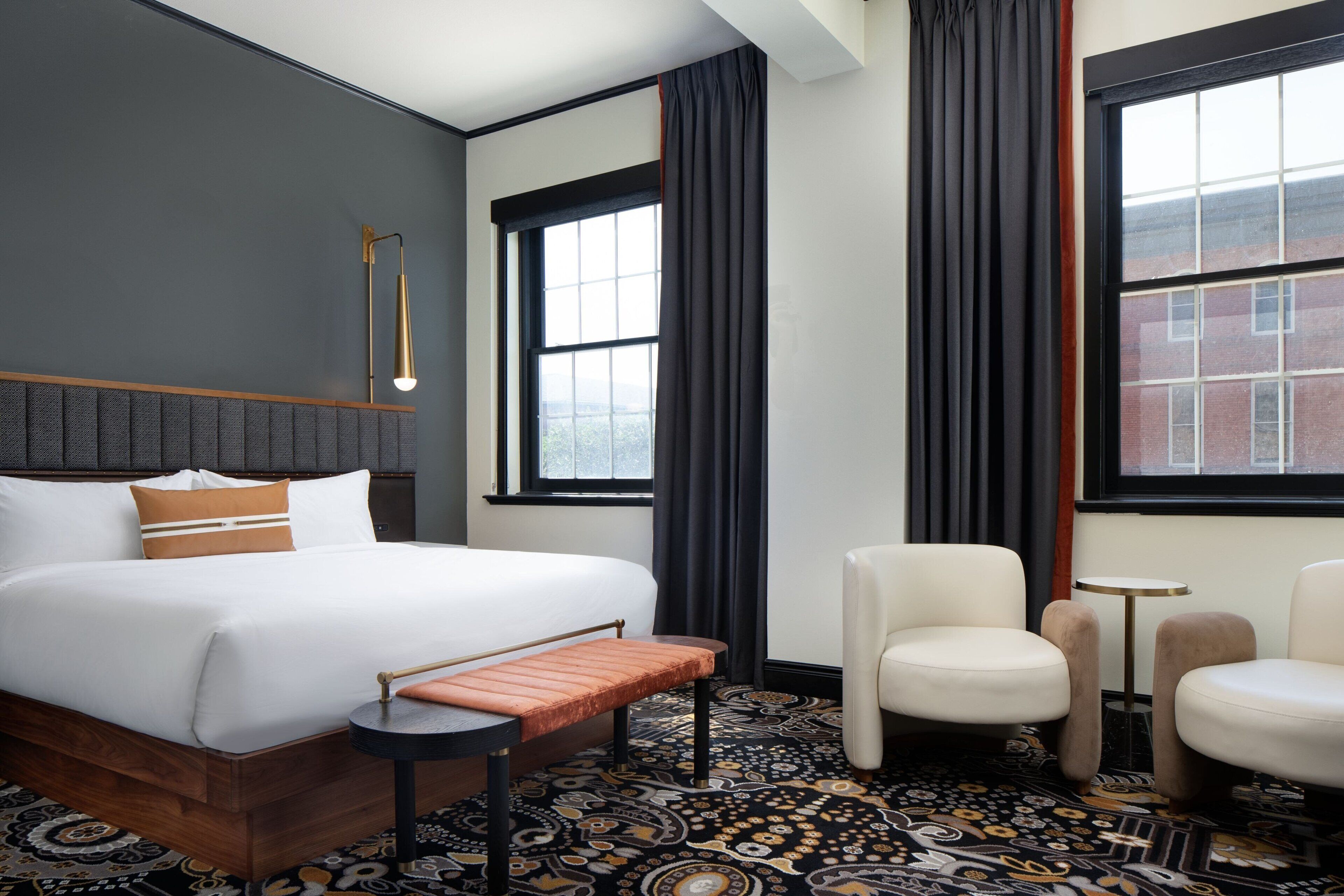 Hotelkamer met een groot bed, twee fauteuils, een tafeltje, een bankje en een kamerbreed tapijt met dessin.