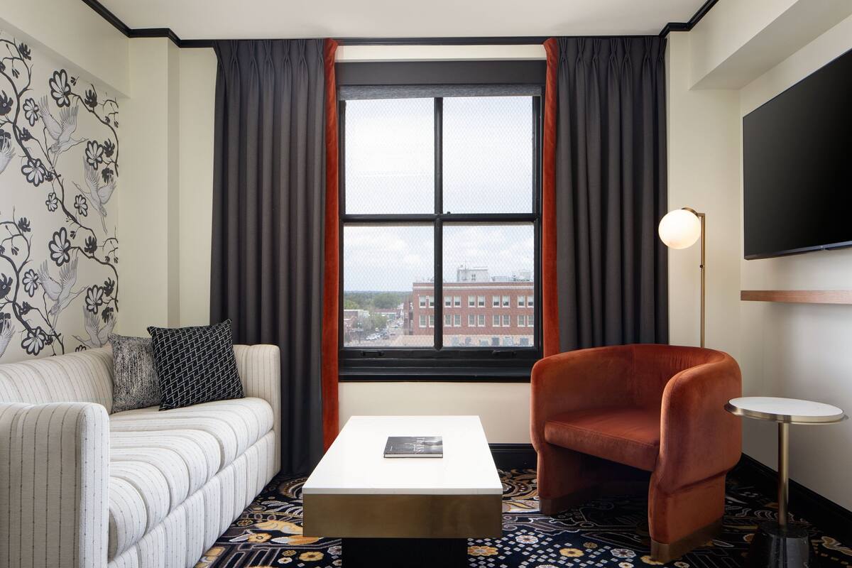 A modern living room with a striped sofa, a round armchair, a small white table, and a large window with curtains.