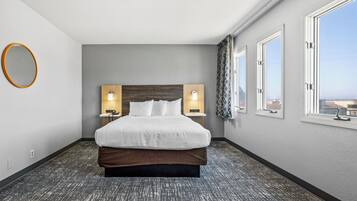 A hotel room with a large bed, two bedside tables with lamps, a round mirror, and a window with a view.