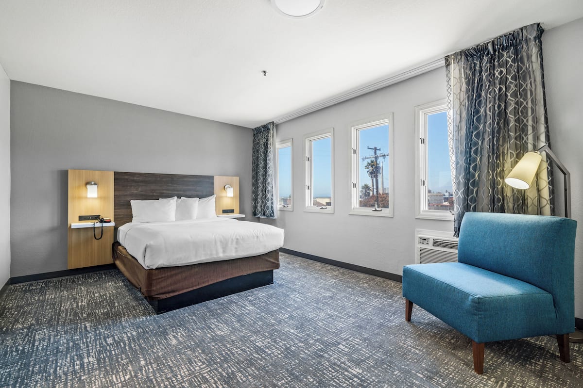 A hotel room with a bed, a chair, a nightstand, and a window with curtains.